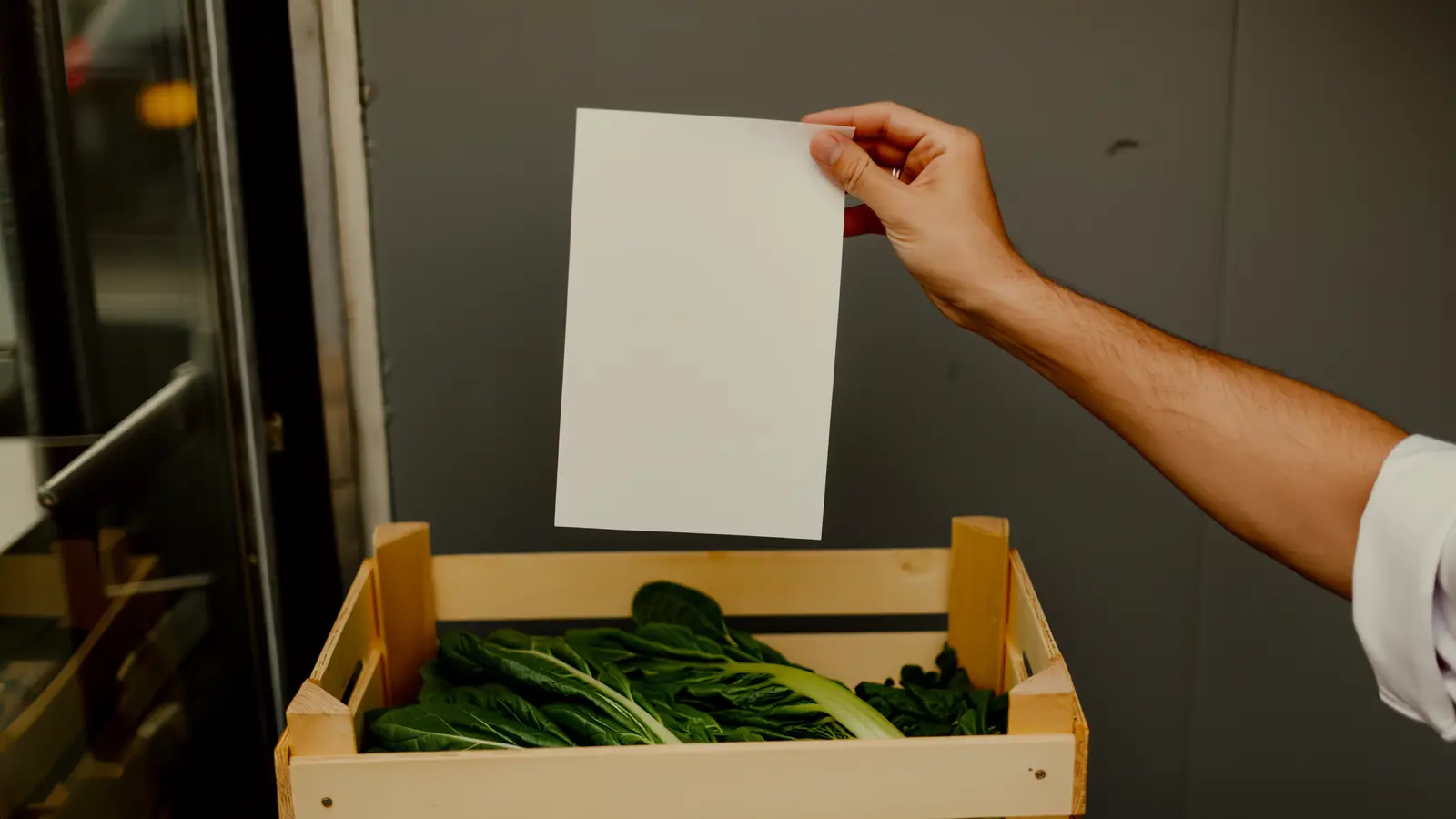 Chef's hands checking a blank delivery note beside an open crate of fresh vegetables in a kitchen