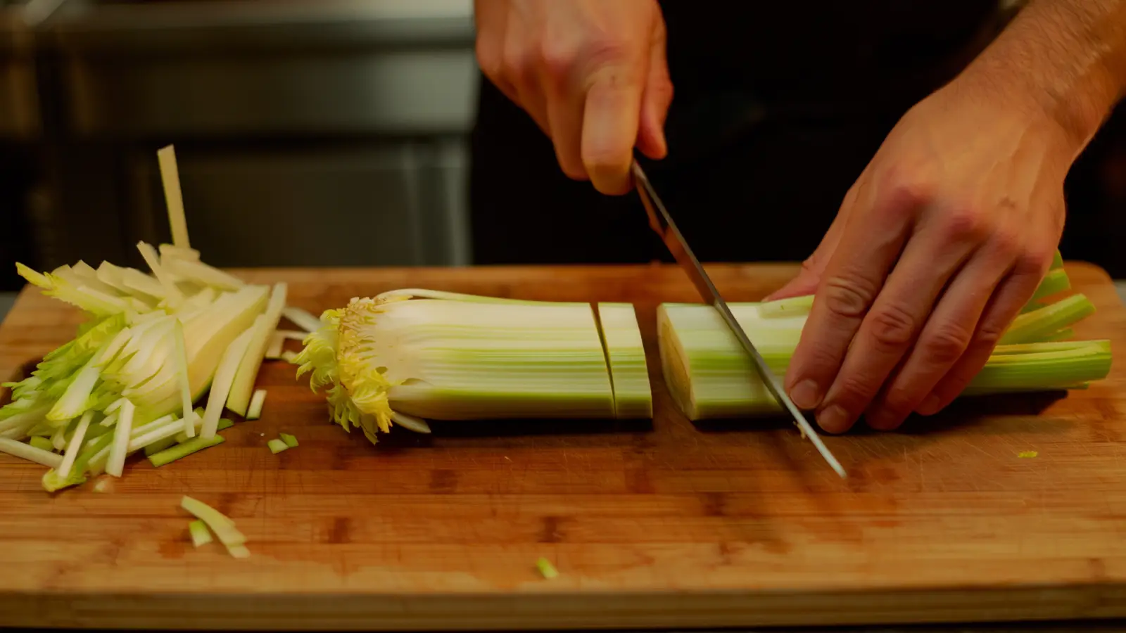 Knife trimming celery on a cutting board, trim gathered to one side